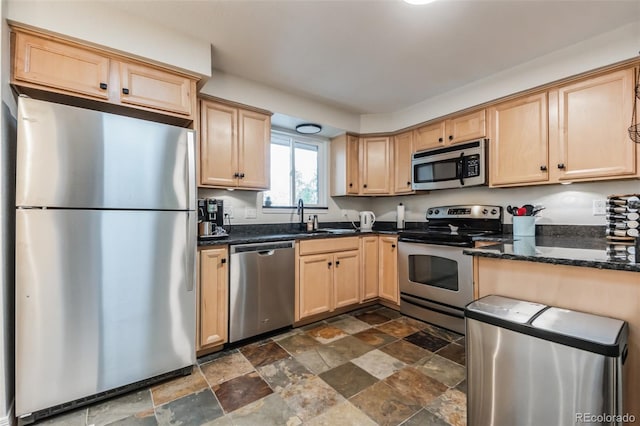 kitchen featuring dark stone counters, stainless steel appliances, light brown cabinetry, and sink