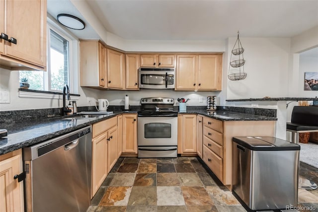 kitchen with appliances with stainless steel finishes, dark stone countertops, light brown cabinetry, and sink