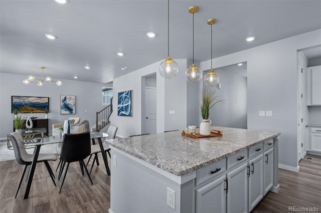 kitchen featuring a center island, hanging light fixtures, hardwood / wood-style flooring, light stone countertops, and white cabinetry