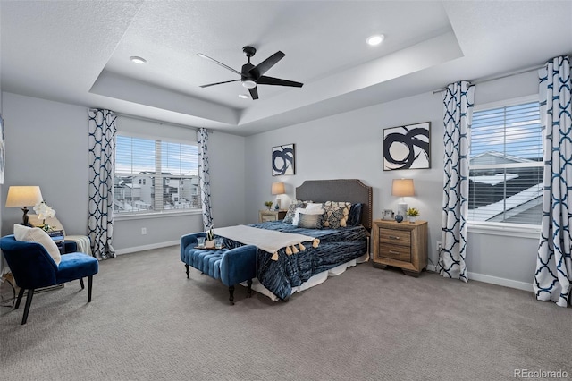 carpeted bedroom with a tray ceiling, baseboards, and ceiling fan