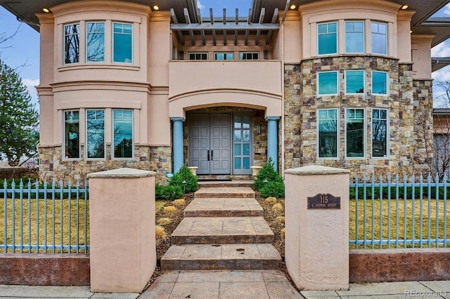 view of front of property with stone siding, a fenced front yard, a front yard, and stucco siding