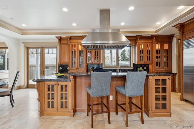 kitchen featuring built in refrigerator, brown cabinets, island range hood, and a raised ceiling