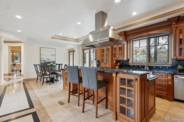 kitchen with island exhaust hood, arched walkways, brown cabinets, and stainless steel dishwasher