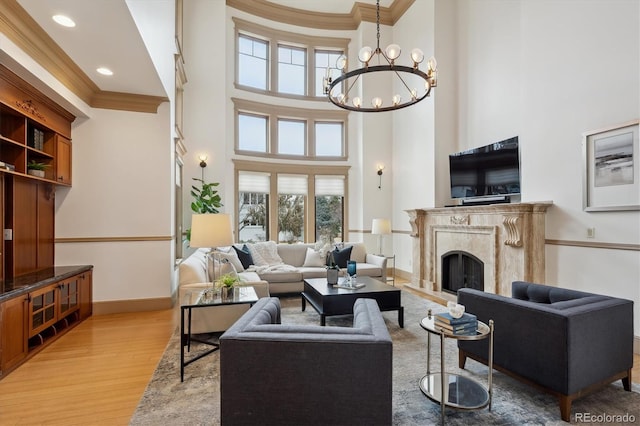 living room with a chandelier, light wood-style flooring, a high end fireplace, baseboards, and ornamental molding