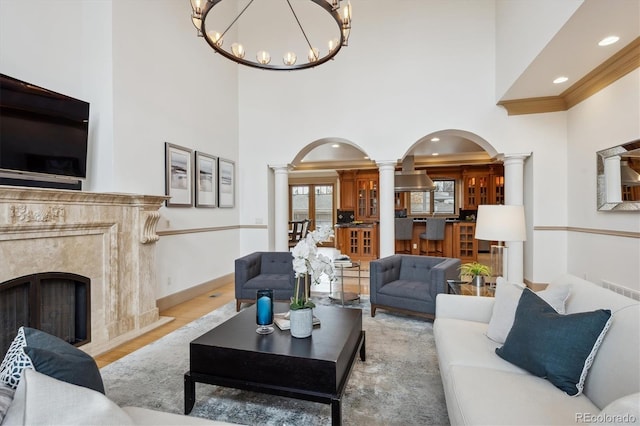 living room with arched walkways, a fireplace, wood finished floors, baseboards, and ornate columns