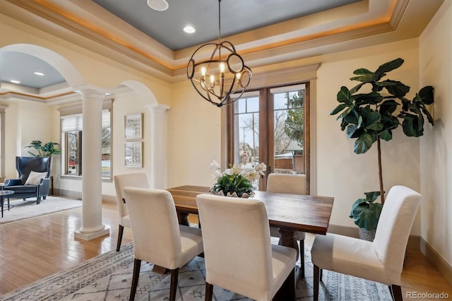 dining space featuring ornate columns, a tray ceiling, arched walkways, and hardwood / wood-style floors