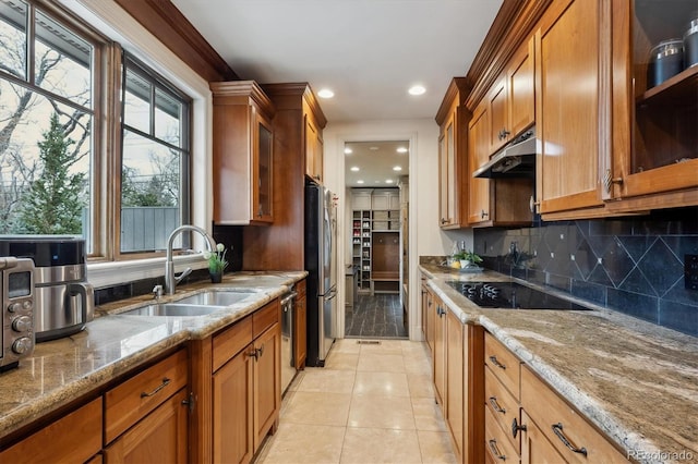 kitchen featuring stainless steel appliances, brown cabinetry, a sink, light stone countertops, and under cabinet range hood