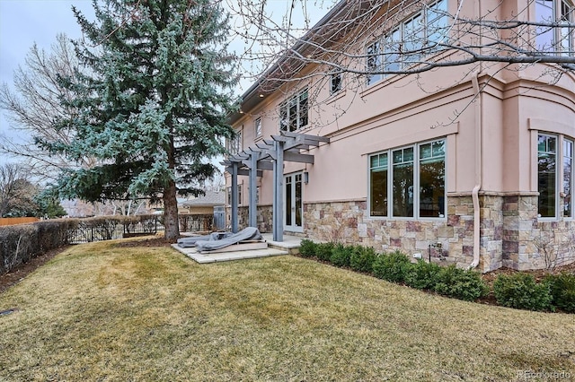 back of house featuring stone siding, fence, a yard, a pergola, and stucco siding