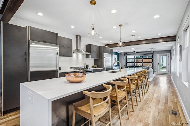 kitchen with a sink, visible vents, stainless steel refrigerator, range, and wall chimney exhaust hood