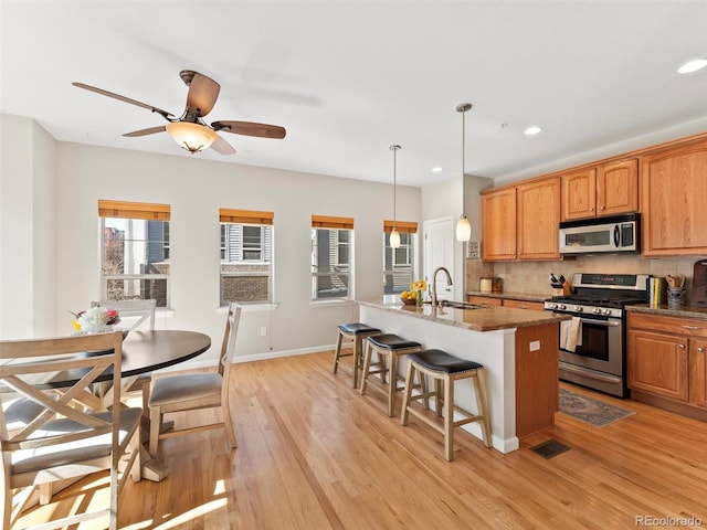 kitchen featuring decorative backsplash, stainless steel appliances, light wood-type flooring, a kitchen bar, and a sink