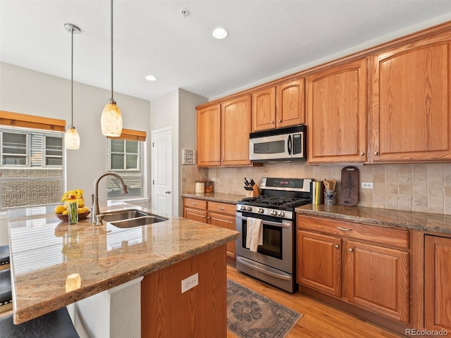 kitchen featuring light stone counters, light wood finished floors, stainless steel appliances, tasteful backsplash, and a sink