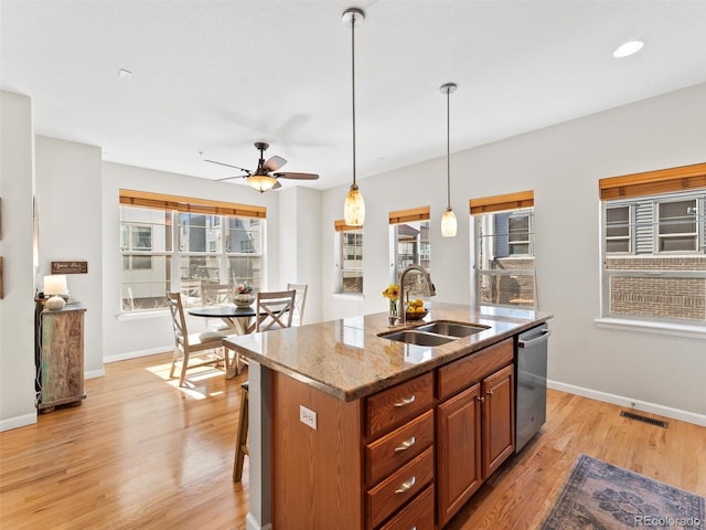 kitchen with light wood finished floors, plenty of natural light, a center island with sink, a sink, and stainless steel dishwasher