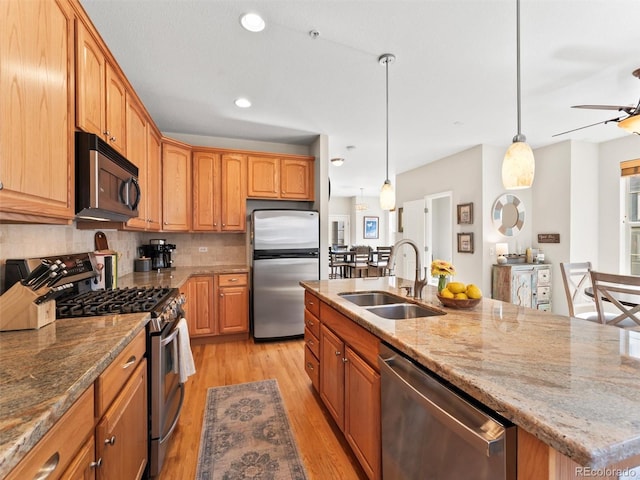 kitchen with light stone countertops, a sink, light wood-style floors, appliances with stainless steel finishes, and decorative backsplash