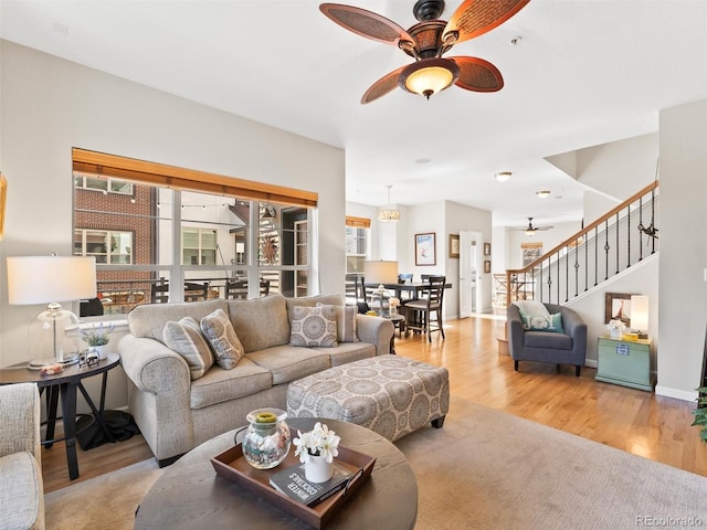 living room featuring a ceiling fan, baseboards, stairway, and wood finished floors