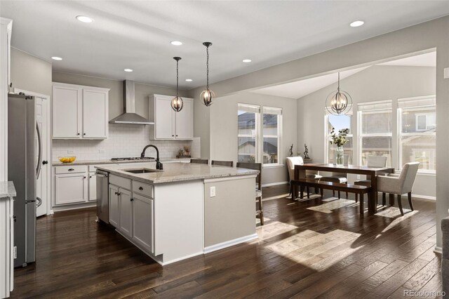 kitchen featuring a center island with sink, wall chimney exhaust hood, decorative light fixtures, and vaulted ceiling