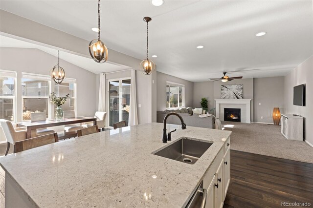 kitchen featuring light stone counters, sink, a center island with sink, hanging light fixtures, and lofted ceiling