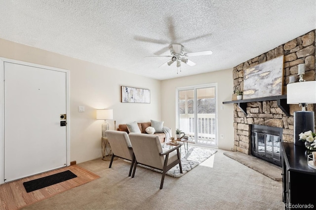 carpeted living room with a textured ceiling, a stone fireplace, and ceiling fan