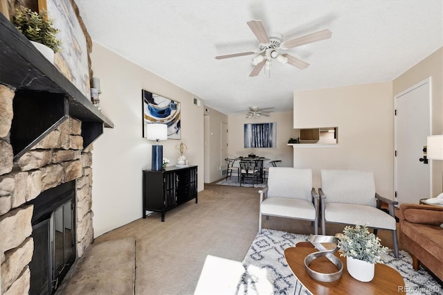 living room featuring light carpet, a fireplace, ceiling fan, and a textured ceiling