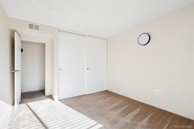 unfurnished bedroom featuring light carpet, a closet, and a textured ceiling