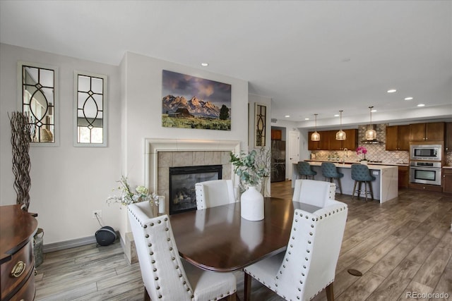 dining space featuring a tiled fireplace, recessed lighting, and wood finished floors