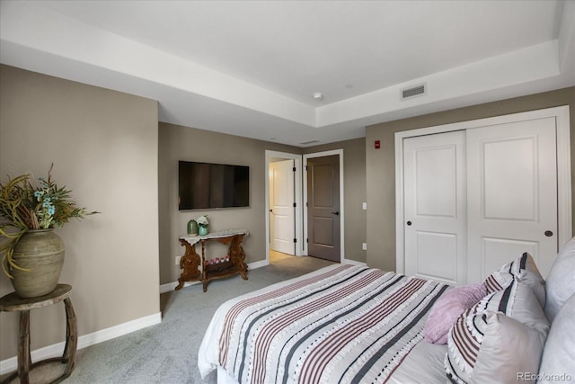 bedroom featuring a closet, a tray ceiling, baseboards, visible vents, and light colored carpet