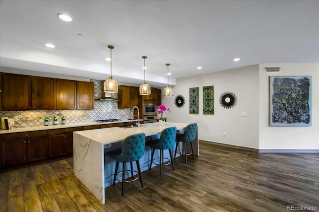 kitchen with stainless steel microwave, tasteful backsplash, visible vents, an island with sink, and dark wood-style floors