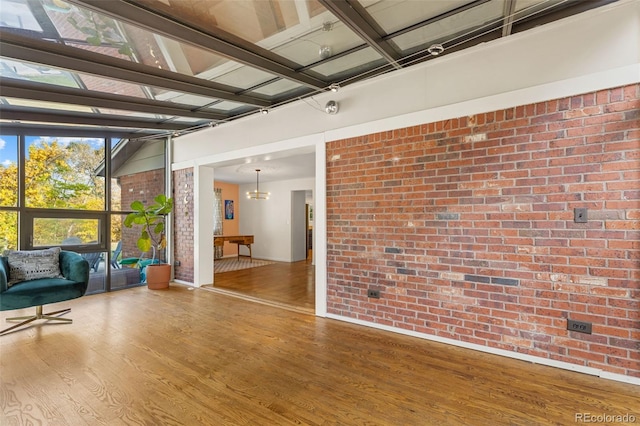 unfurnished room featuring a notable chandelier, hardwood / wood-style flooring, and brick wall