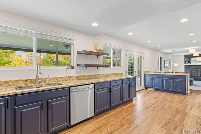 kitchen with sink, light stone countertops, a brick fireplace, light wood-type flooring, and stainless steel dishwasher