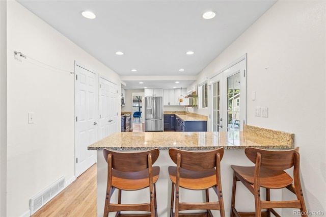 kitchen featuring appliances with stainless steel finishes, kitchen peninsula, a kitchen breakfast bar, white cabinets, and blue cabinetry