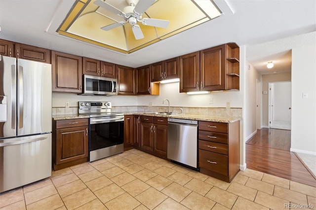 kitchen featuring ceiling fan, sink, stainless steel appliances, light stone counters, and light hardwood / wood-style flooring