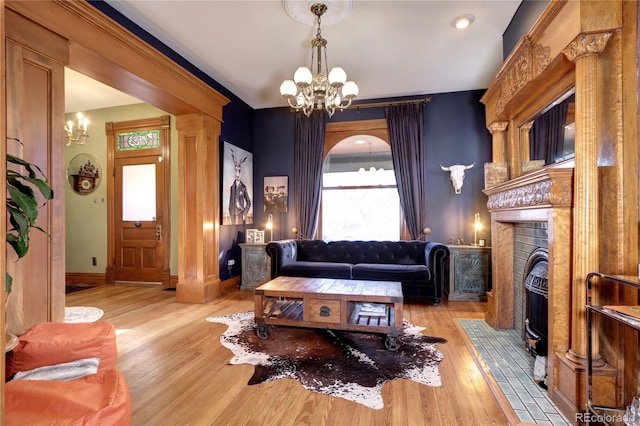 living room with a notable chandelier, ornate columns, a fireplace, and light hardwood / wood-style flooring