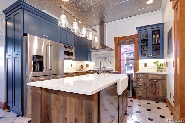 kitchen with stainless steel appliances, wall chimney range hood, backsplash, crown molding, and a center island with sink