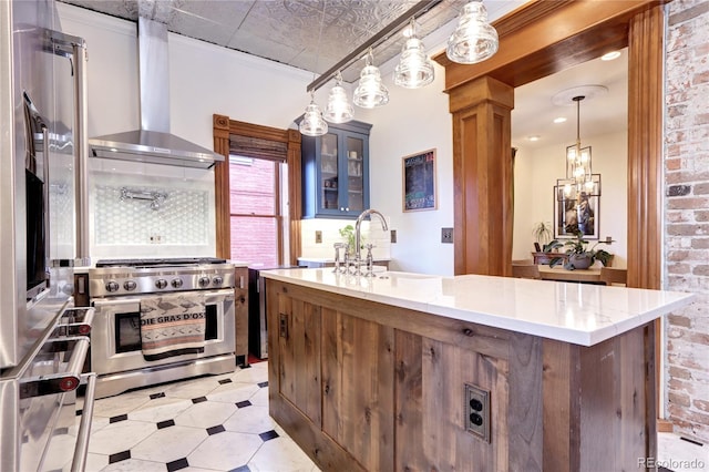 kitchen featuring pendant lighting, a center island with sink, range with two ovens, sink, and wall chimney exhaust hood