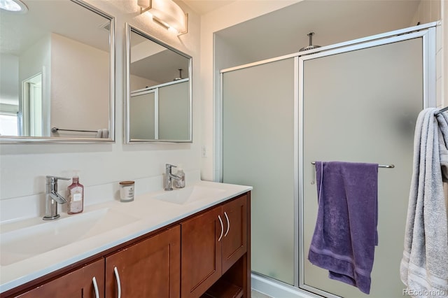 bathroom featuring double vanity, a stall shower, and a sink