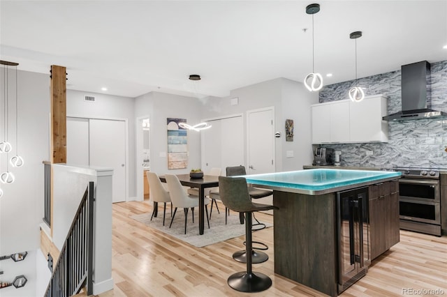kitchen with wall chimney range hood, white cabinets, light wood-style floors, double oven range, and wine cooler