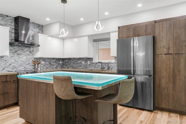 kitchen featuring a kitchen island, wall chimney exhaust hood, white cabinets, a sink, and stainless steel appliances
