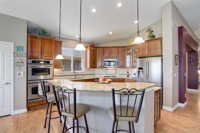 14879 Xenia St, Thornton, CO 80602 - kitchen featuring appliances with stainless steel finishes, a sink, brown cabinetry, a kitchen island, and vaulted ceiling