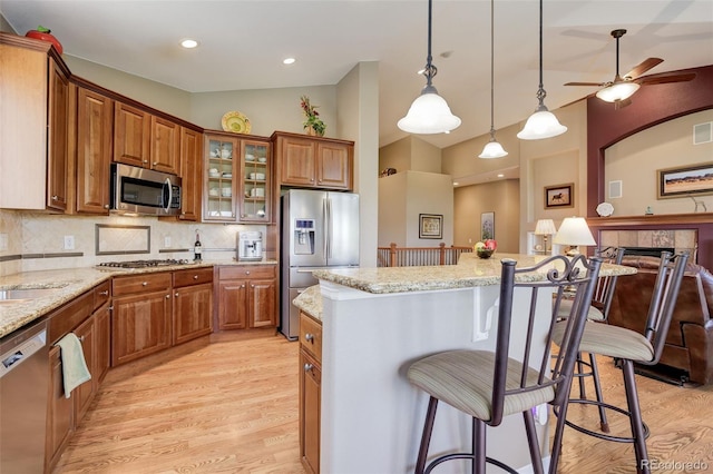 14879 Xenia St, Thornton, CO 80602 - kitchen featuring appliances with stainless steel finishes, brown cabinets, a breakfast bar, light wood-style floors, and high vaulted ceiling