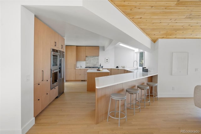 kitchen with light hardwood / wood-style floors, kitchen peninsula, a breakfast bar area, sink, and stainless steel double oven