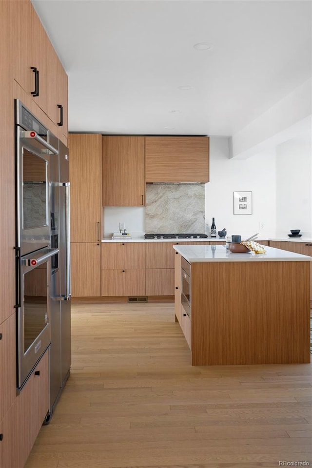 kitchen with gas stovetop, decorative backsplash, light hardwood / wood-style floors, double oven, and a center island