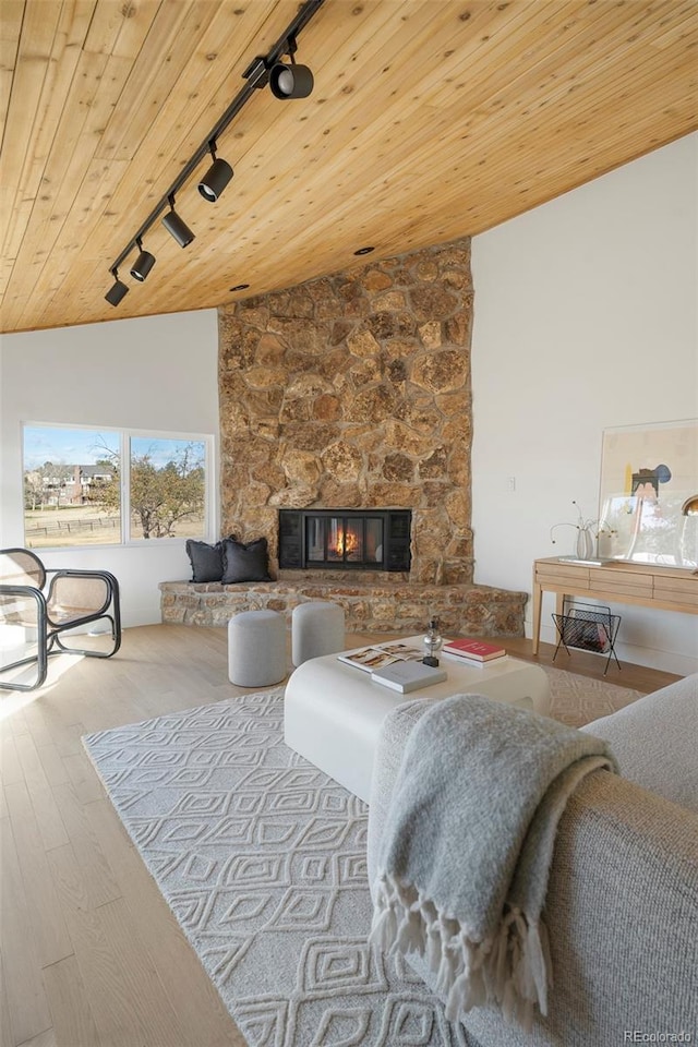 living room with a stone fireplace, track lighting, wood ceiling, lofted ceiling, and light hardwood / wood-style flooring