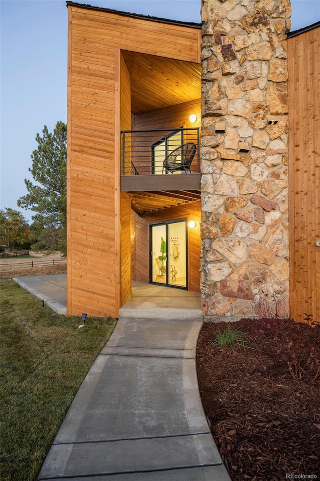 exterior entry at dusk featuring a lawn and a balcony