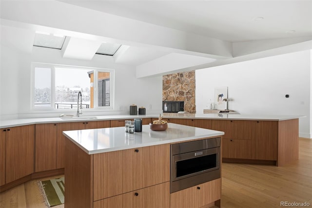 kitchen featuring a center island, a stone fireplace, sink, stainless steel microwave, and light hardwood / wood-style flooring