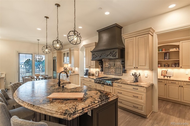 kitchen featuring light stone countertops, premium range hood, stainless steel gas stovetop, a center island with sink, and a breakfast bar area