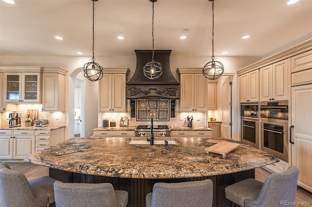 kitchen with custom exhaust hood, hanging light fixtures, a kitchen island with sink, sink, and a breakfast bar area