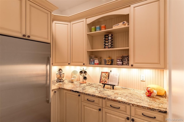 bar with built in refrigerator, light stone counters, cream cabinetry, and tasteful backsplash