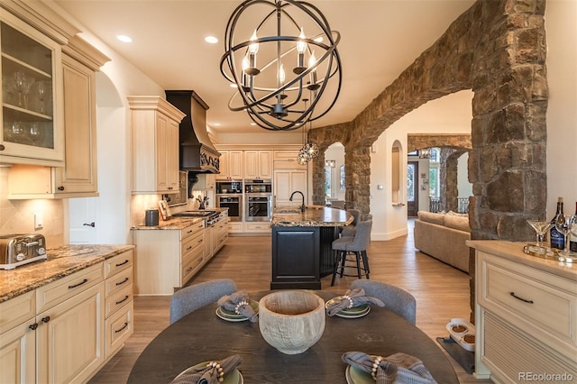 kitchen with light stone countertops, hardwood / wood-style flooring, custom range hood, hanging light fixtures, and a kitchen breakfast bar