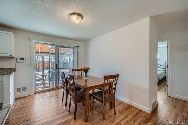 dining room featuring a textured ceiling, light wood finished floors, visible vents, and baseboards