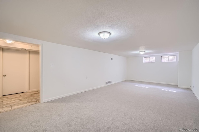 basement with a textured ceiling, baseboards, visible vents, and light colored carpet