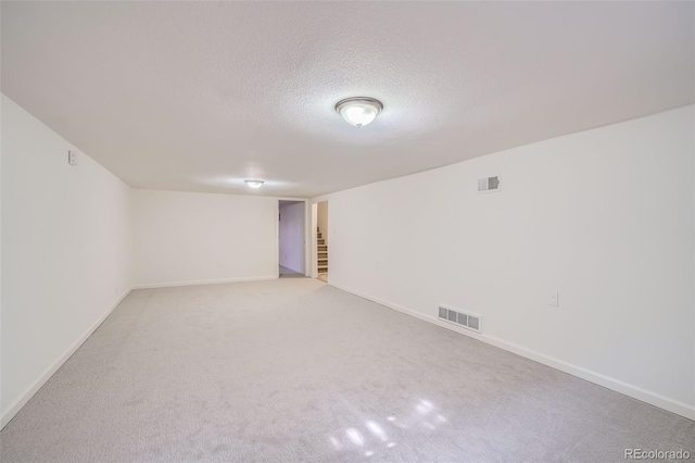 spare room featuring a textured ceiling, light carpet, visible vents, baseboards, and stairs